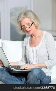 Senior woman sitting in sofa with laptop computer