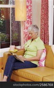 Senior woman sitting on a couch and reading a book
