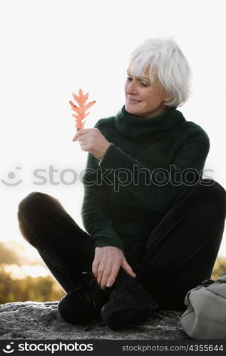 Senior woman sitting on a rock and looking at a leaf