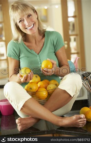 Senior Woman Sitting On Kitchen Counter With Bowl Of Oranges