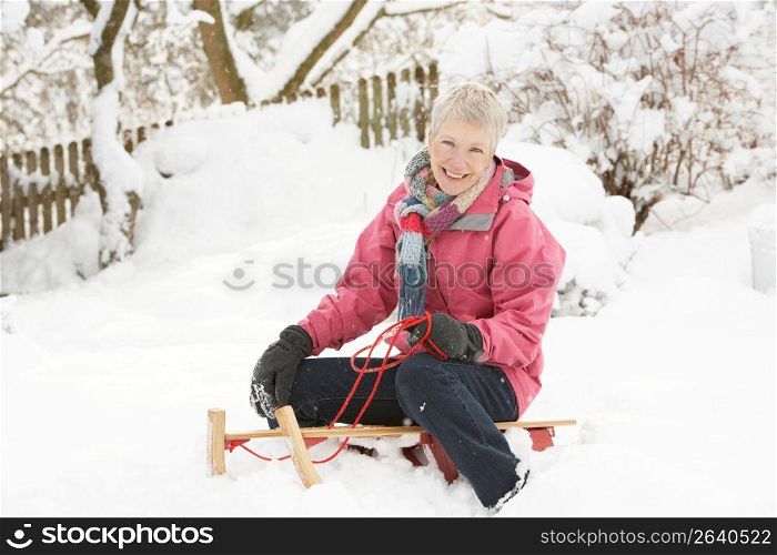 Senior Woman Sitting On Sledge In Snowy Landscape