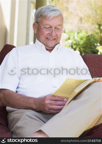 Senior woman sitting outdoors on a chair reading a book