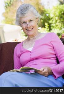 Senior woman sitting outdoors on a chair reading a book