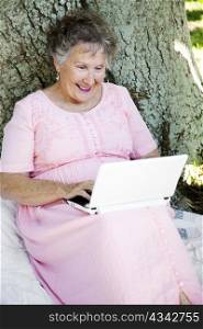 Senior woman sitting outdoors reading her e-mail on a netbook computer.