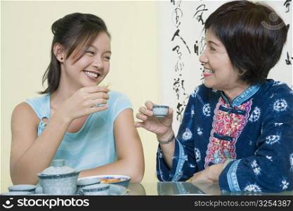 Senior woman sitting with her granddaughter at a table and holding tea cups