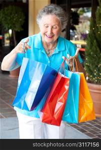 Senior woman smiles as she looks into her shopping bags to check out what she&rsquo;s bought.
