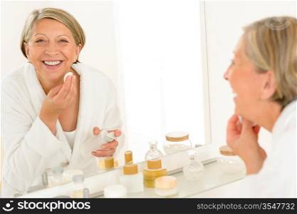 Senior woman smiling cleaning face make-up removal bathroom mirror reflection