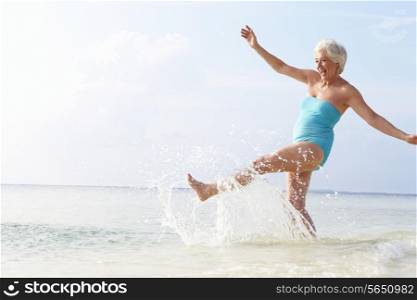 Senior Woman Splashing In Sea On Beach Holiday