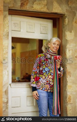 Senior woman standing in a doorway and holding a cup