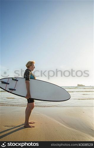 Senior woman standing on beach with surfboard, Camaret-sur-mer, Brittany, France