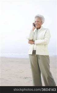 Senior woman stands on beach talking on mobile phone
