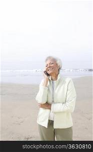 Senior woman stands on beach talking on mobile phone