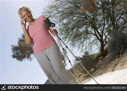 Senior woman stands on phone with walking poles