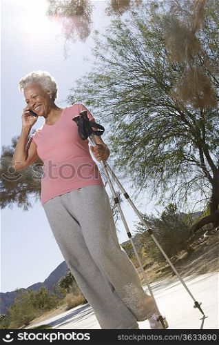 Senior woman stands on phone with walking poles