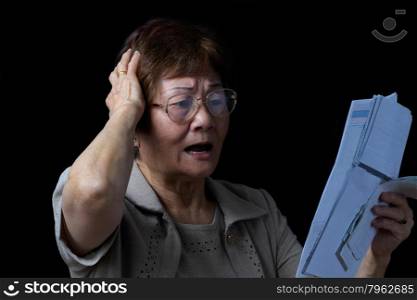 Senior woman stressed out by looking at her bills. Black background.