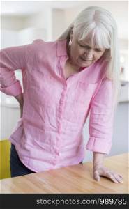 Senior Woman Suffering From Backache Whilst Getting Out Of Chair At Home