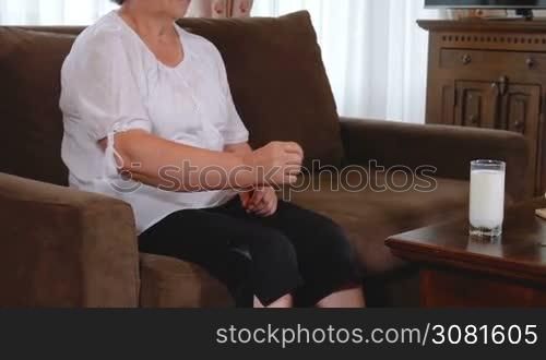 Senior woman suffering from elbow pain at home. Old age, health problem and people concept. She wants to drink milk for calcium bones health. Slow motion hand held movement