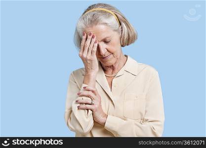 Senior woman suffering from headache against blue background