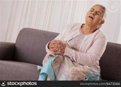 Senior woman suffering from knee pain while sitting on sofa