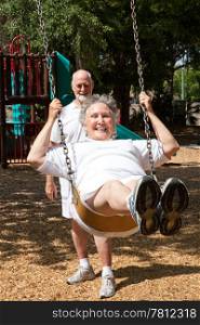 Senior woman swinging on the playground in the park. Her husband is pushing her.