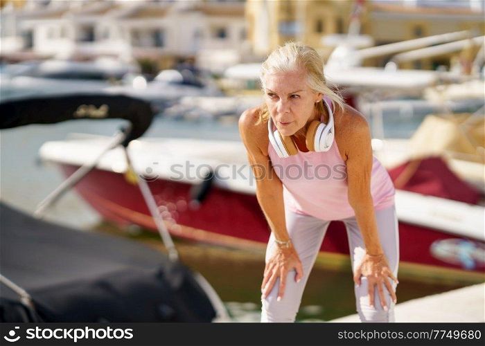 Senior woman taking a break during exercise. Concept of healthy living in the elderly. Mature sportswoman in fitness clothing. Older female doing sport to keep fit.. Mature sportswoman in fitness clothing taking a break during exercise.