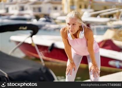 Senior woman taking a break during exercise. Concept of healthy living in the elderly. Mature sportswoman in fitness clothing. Older female doing sport to keep fit.. Mature sportswoman in fitness clothing taking a break during exercise.