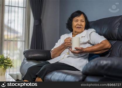 senior woman talking and drinking a cup of water in living room