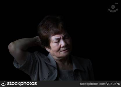 Senior woman touching the back of her head while displaying pain on black background.