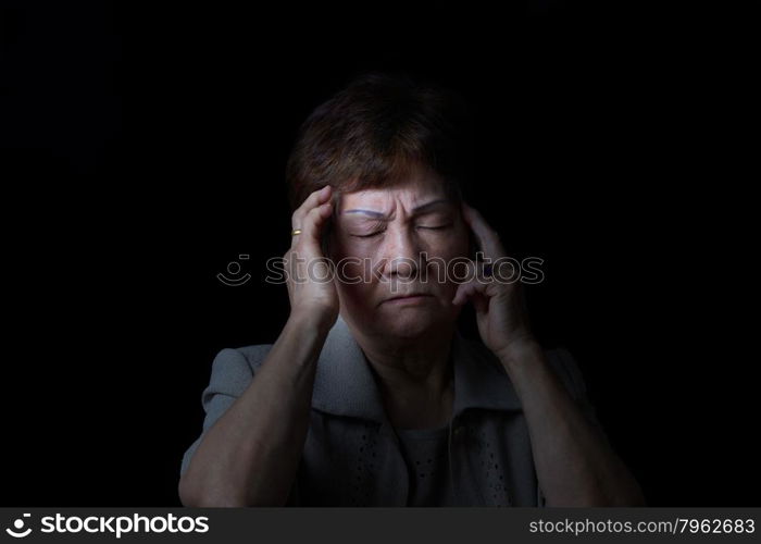 Senior woman touching the sides of her head with fingers while displaying pain on black background.