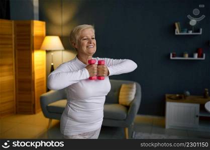 Senior woman training with dumbbell at home. Fitness training on quarantine. Body care on retirement. Senior woman training with dumbbells at home