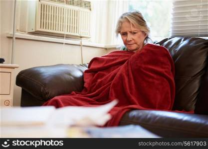 Senior Woman Trying To Keep Warm Under Blanket At Home