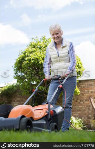 Senior Woman Using Electric Lawn Mower To Cut Grass At Home