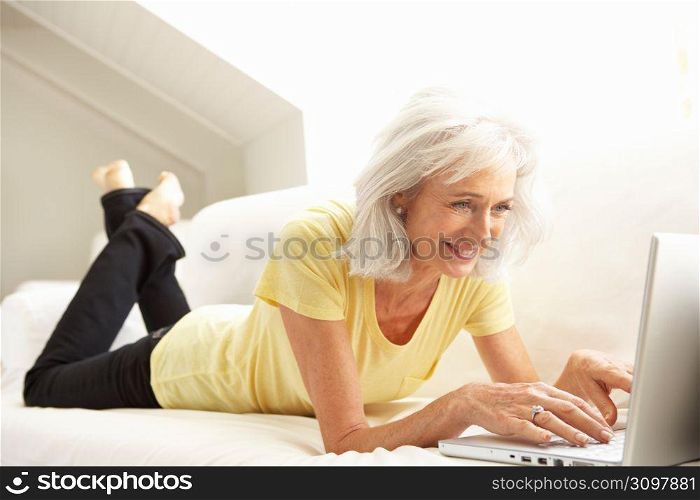 Senior Woman Using Laptop Relaxing Sitting On Sofa At Home