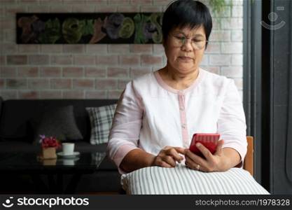 senior woman using mobile phone while sitting on sofa at home