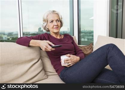 Senior woman using TV remote control on sofa at home