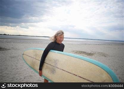 Senior woman walking from sea, carrying surfboard