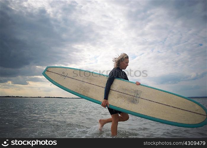 Senior woman walking from sea, carrying surfboard