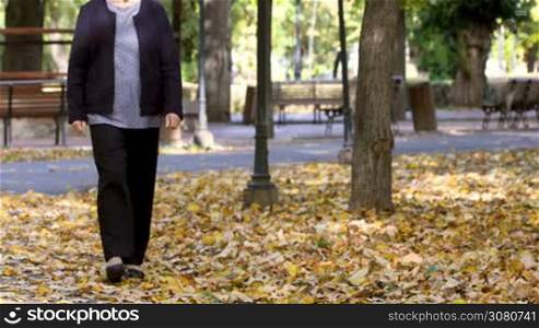 Senior woman walking in autumn park and having knee pain. Arthritis pain concept. The person comes in focus.