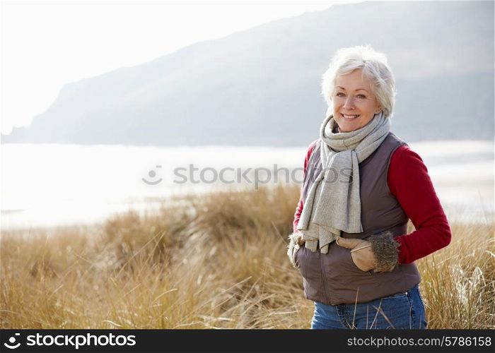 Senior Woman Walking Through Sand Dunes On Winter Beach