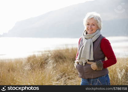 Senior Woman Walking Through Sand Dunes On Winter Beach