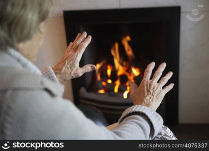 Senior Woman Warming Hands By Fire At Home