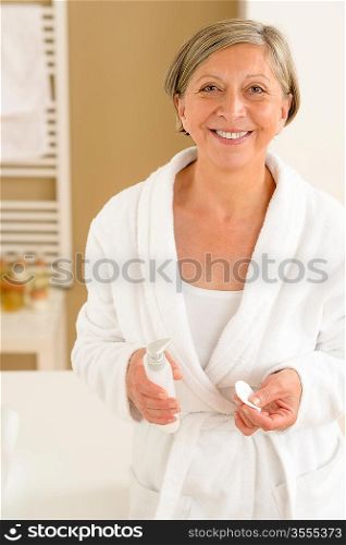 Senior woman wear bathrobe standing in bathroom with hygiene products
