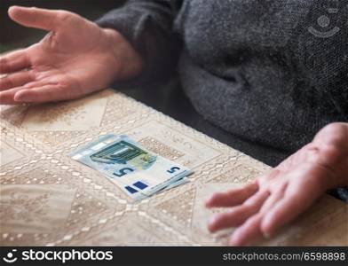 Senior woman with 5 euro on table, cost of living, minimal income pensioner concept