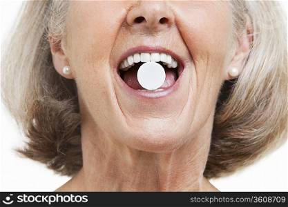 Senior woman with a pill between her teeth against white background