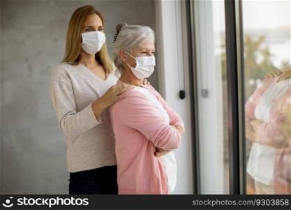 Senior woman with caring daughter at home wearing medical masks as a protection from coronavirus
