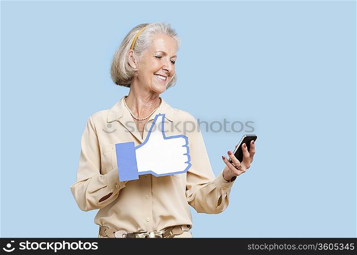 Senior woman with cell phone holding fake like button against blue background
