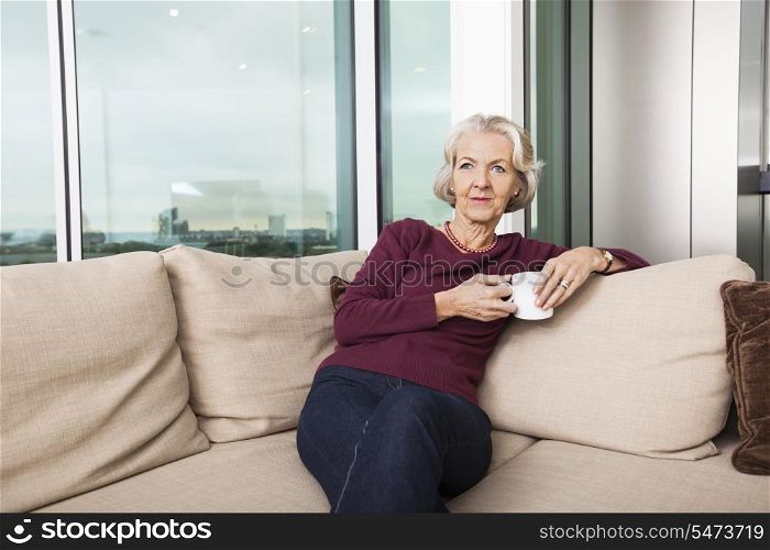 Senior woman with coffee mug sitting on sofa at home