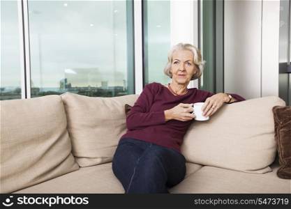 Senior woman with coffee mug sitting on sofa at home