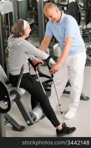 Senior woman with crutches getting help of physiotherapist at gym