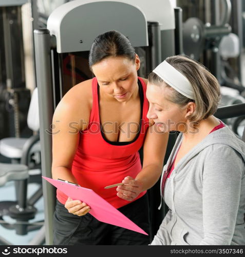 Senior woman with personal trainer looking exercise chart at gym